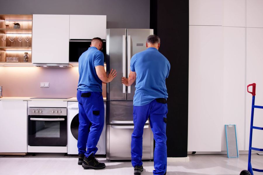 Two CARE crew members installing a refrigerator in a customer kitchen